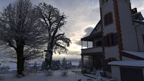 Paisaje nevado con un árbol grande y un edificio con una torre.