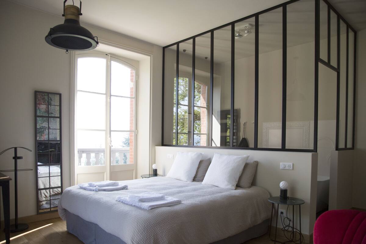A bedroom with a large bed, a window, a mirror, and a red chair.
