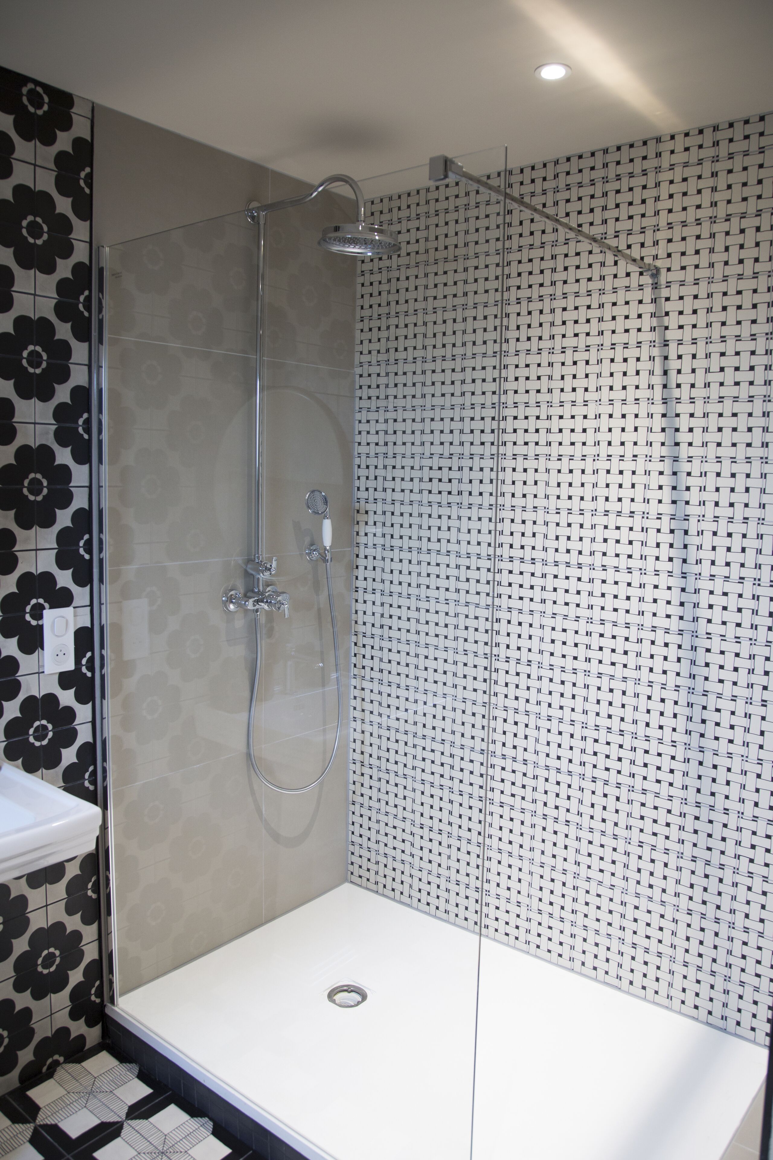 Une salle de bain moderne avec une douche à parois de verre, un lavabo blanc et des carreaux décoratifs sur les murs.