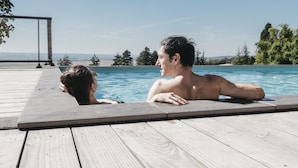 Terraza de madera con piscina, cielo despejado y árboles a lo lejos.