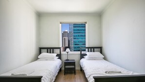 A small, clean room with two single beds, a nightstand, and a window with a city view. - 3 Bedrooms 2 Car Parks Carlton Garden Opposite (Melbourne)