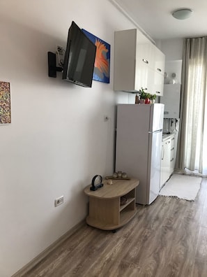 A compact kitchen with a refrigerator, a microwave, and a small table with a clock and decorative items.