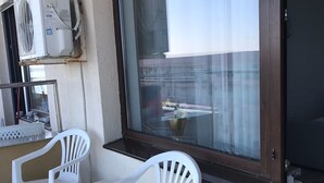 A balcony with two white plastic chairs, a window with a view of buildings, and air conditioning units mounted on the wall. - Sea View Studio Mamaia (Constanta)