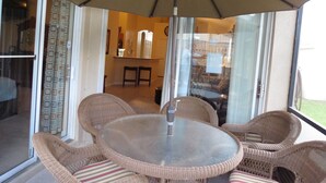 Un patio al aire libre con muebles de mimbre, una mesa de vidrio y un paraguas grande.