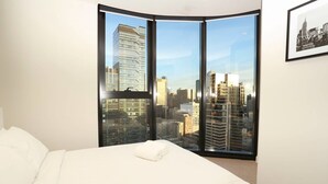 A hotel room with a bed, a large window with a city view, and a framed picture on the wall. - Central But Quiet Apartment (Melbourne)