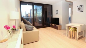 A modern living room with a sofa, a TV, a small table, and a chair. - Central But Quiet Apartment (Melbourne)