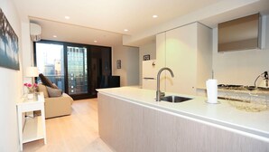A modern kitchen with a central island, a built-in sink, and a dining area with a sofa and table. - Central But Quiet Apartment (Melbourne)