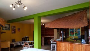 A cozy restaurant interior with wooden tables and benches, a thatched roof bar, and a green accent wall. - Swakopmund Backpackers (Swakopmund)