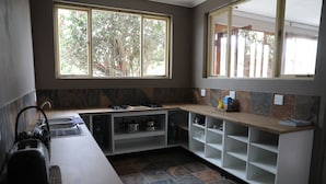 A kitchen with a gas stove, a sink, and a window with a view of trees. - Swakopmund Backpackers (Swakopmund)