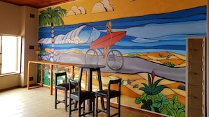 A dining area with a mural of a beach scene, wooden ceiling, and tiled floor. - Swakopmund Backpackers (Swakopmund)
