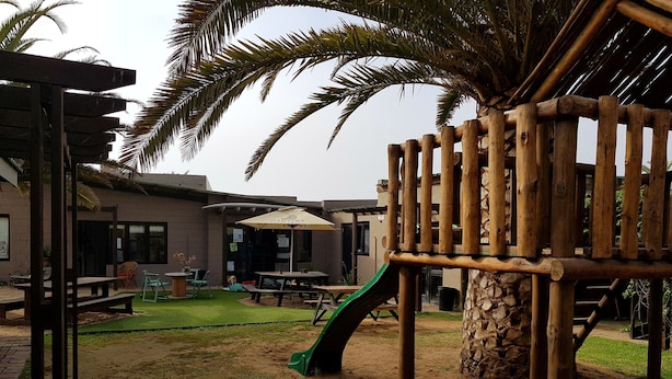 A playground with a slide and climbing structure, surrounded by a patio area with tables and chairs. - Swakopmund Backpackers (Swakopmund)