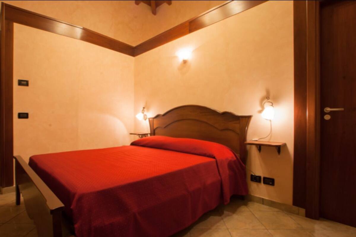 Een hotelkamer met een bed, twee bedlampjes, een houten hoofdbord en een deur.