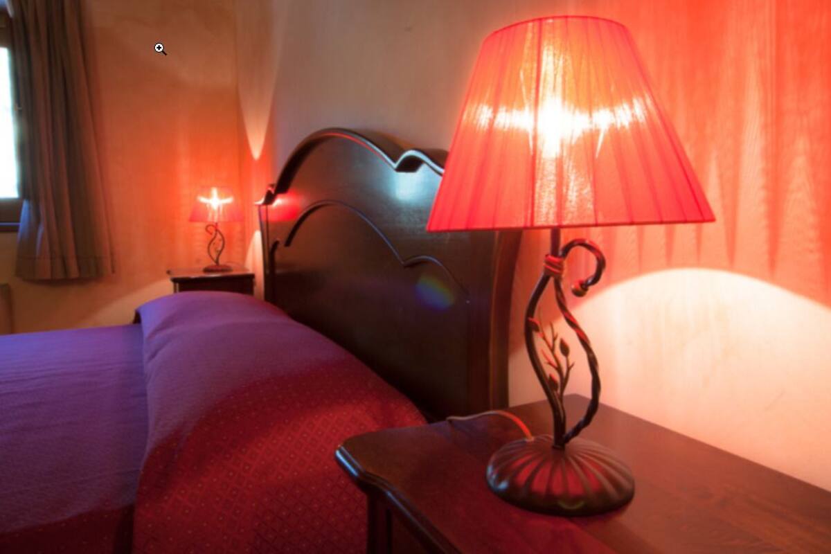 Een bed met een rode deken, een nachtkastje met een rode lamp en een raam met gordijnen.