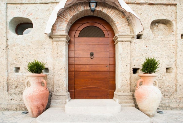 A wooden door with a brick archway, flanked by two large terracotta pots with plants.