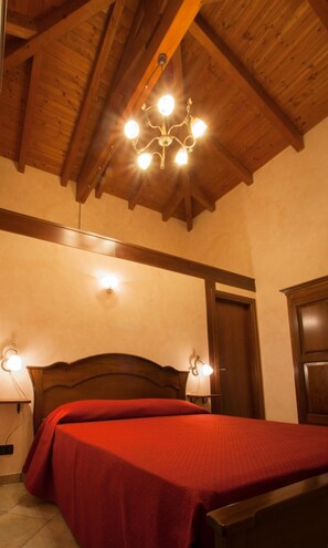 Una habitación con techo de madera, una cama con colcha roja, dos lámparas de noche y un aplique de pared.