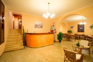 Un hall de hotel con mostrador de recepción, una escalera y un comedor con mesas y sillas.