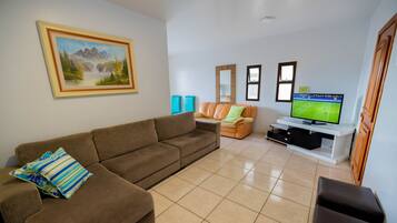 A living room with a brown sofa, a smaller orange sofa, a TV on a white stand, and a painting on the wall.