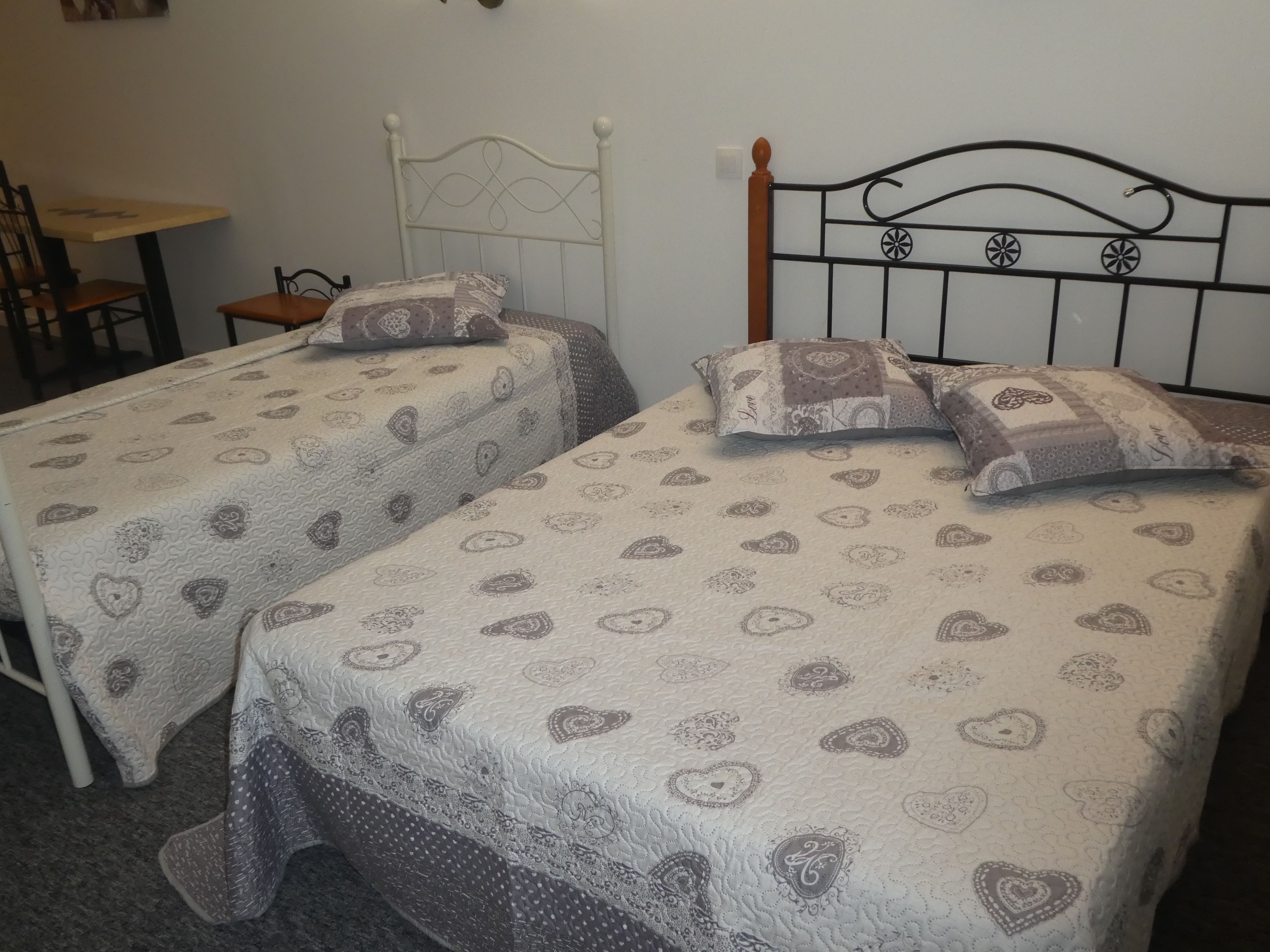 A room with two single beds, each with patterned bedding and pillows, a wooden nightstand, and a small table.