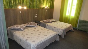 A room with two single beds, each with patterned bedding and pillows, a wooden headboard, and a green wall with vertical lines. - Phoenix Hôtel (Béziers)