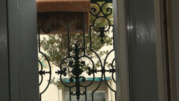A view through a balcony door with a wrought iron railing, a small hanging plant, and a building with a turret and tiled roof in the background. - Phoenix Hôtel (Béziers)