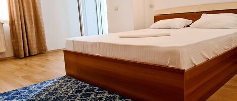 A bedroom with a wooden bed, white bedding, and a patterned rug.