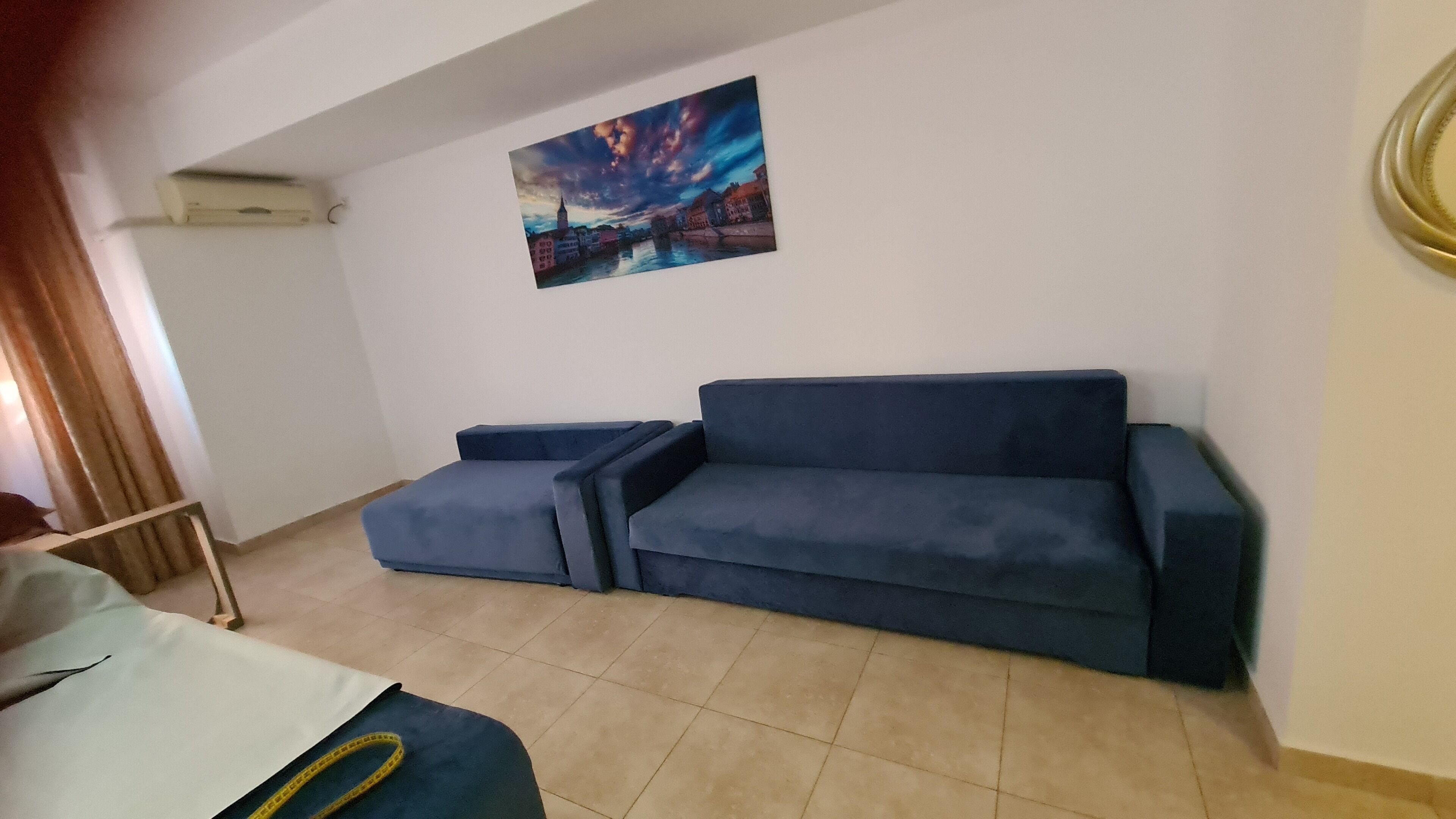Un salon avec un canapé bleu, une petite table et un tableau représentant un paysage urbain accroché au mur.