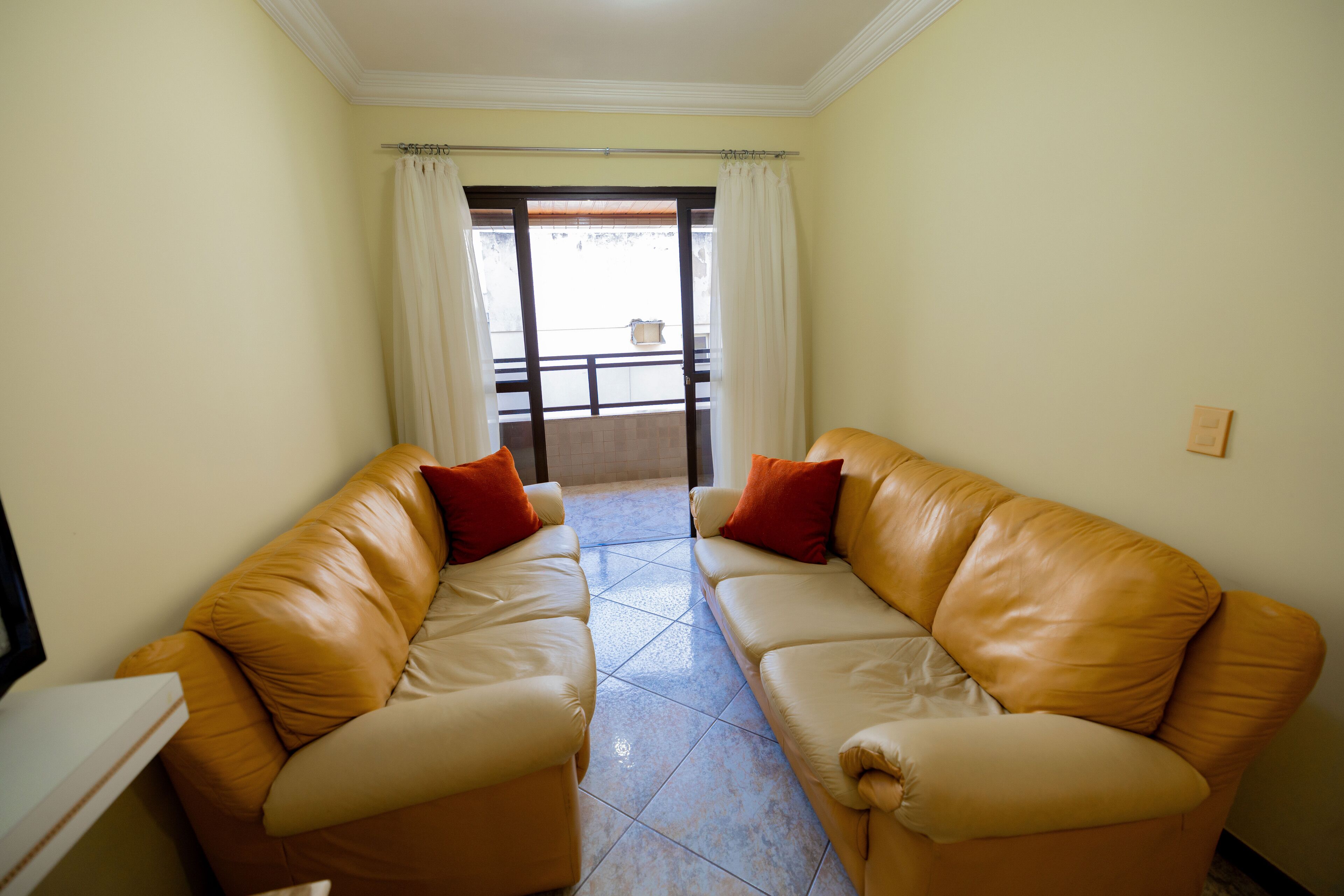 A living room with two leather sofas, a small table, and a sliding glass door leading to a balcony.