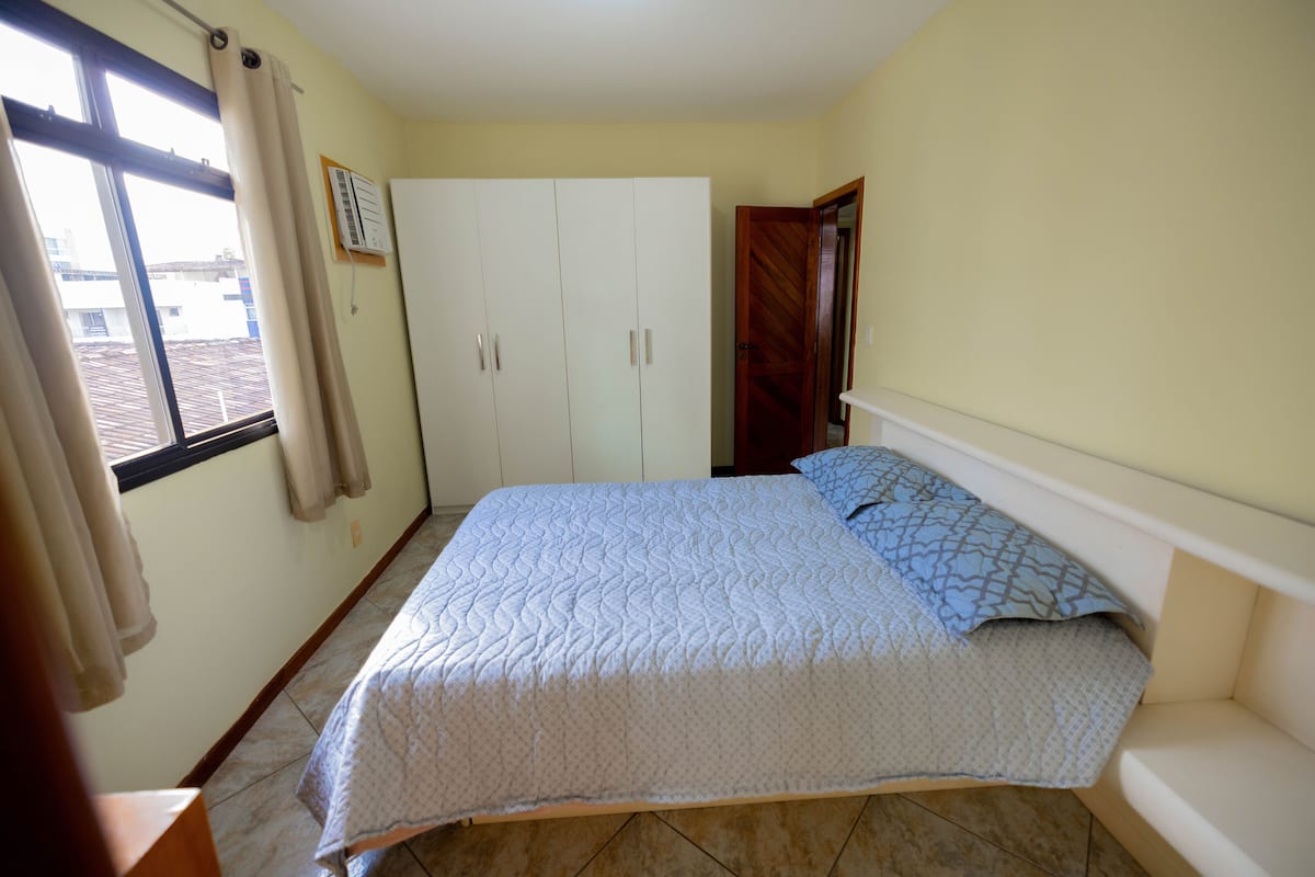 Ein Schlafzimmer mit Bett, Kleiderschrank und einem Fenster mit Vorhängen.