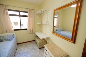 Ein Schlafzimmer mit Bett, Schreibtisch, Kommode, Spiegel und einem Fenster mit Vorhängen.