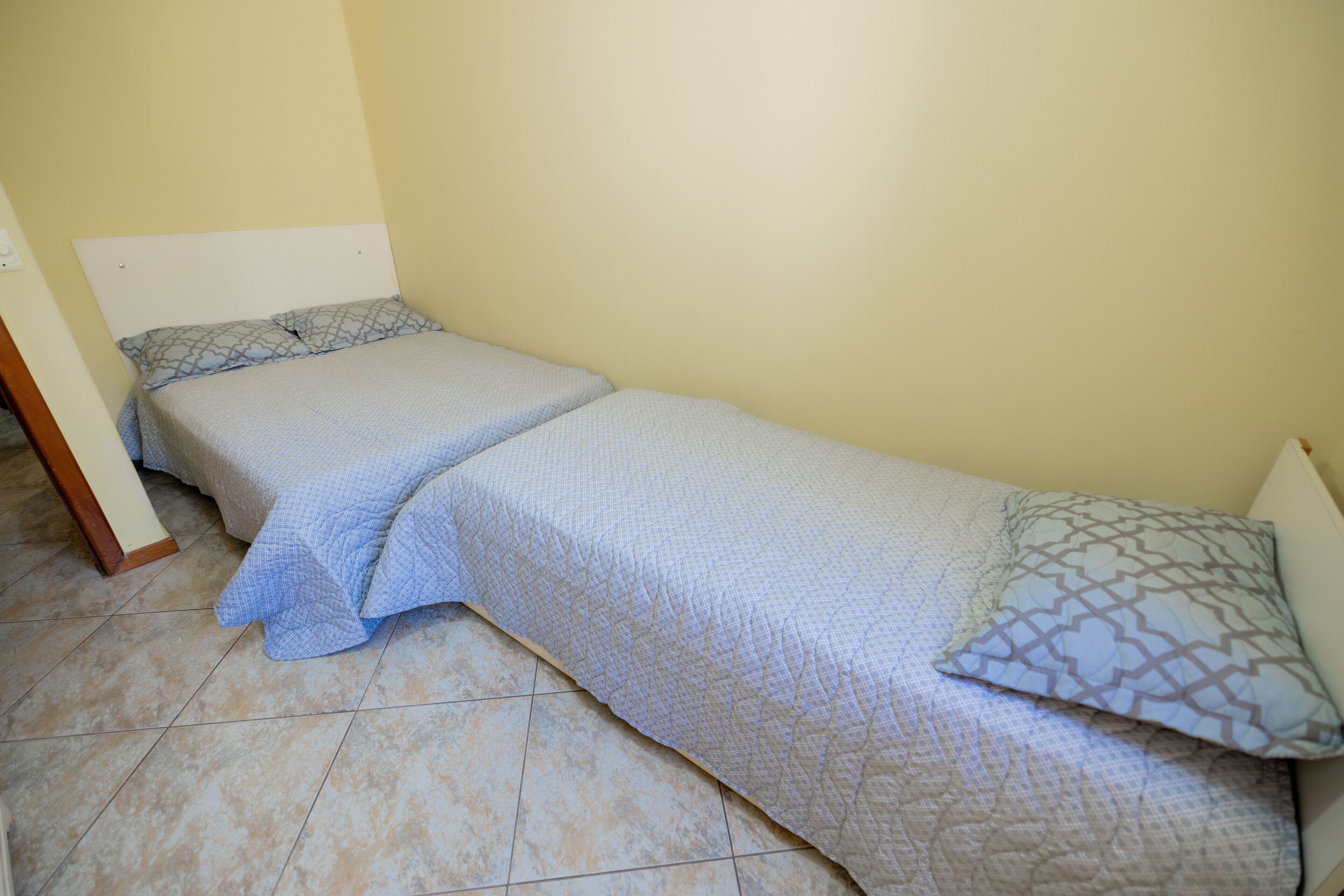 Una habitación pequeña con cama individual, cabecera sencilla y almohada estampada.