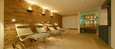 Una habitación con cuatro sillones reclinables frente a una pared de piedra, un separador de vidrio y un techo de madera.