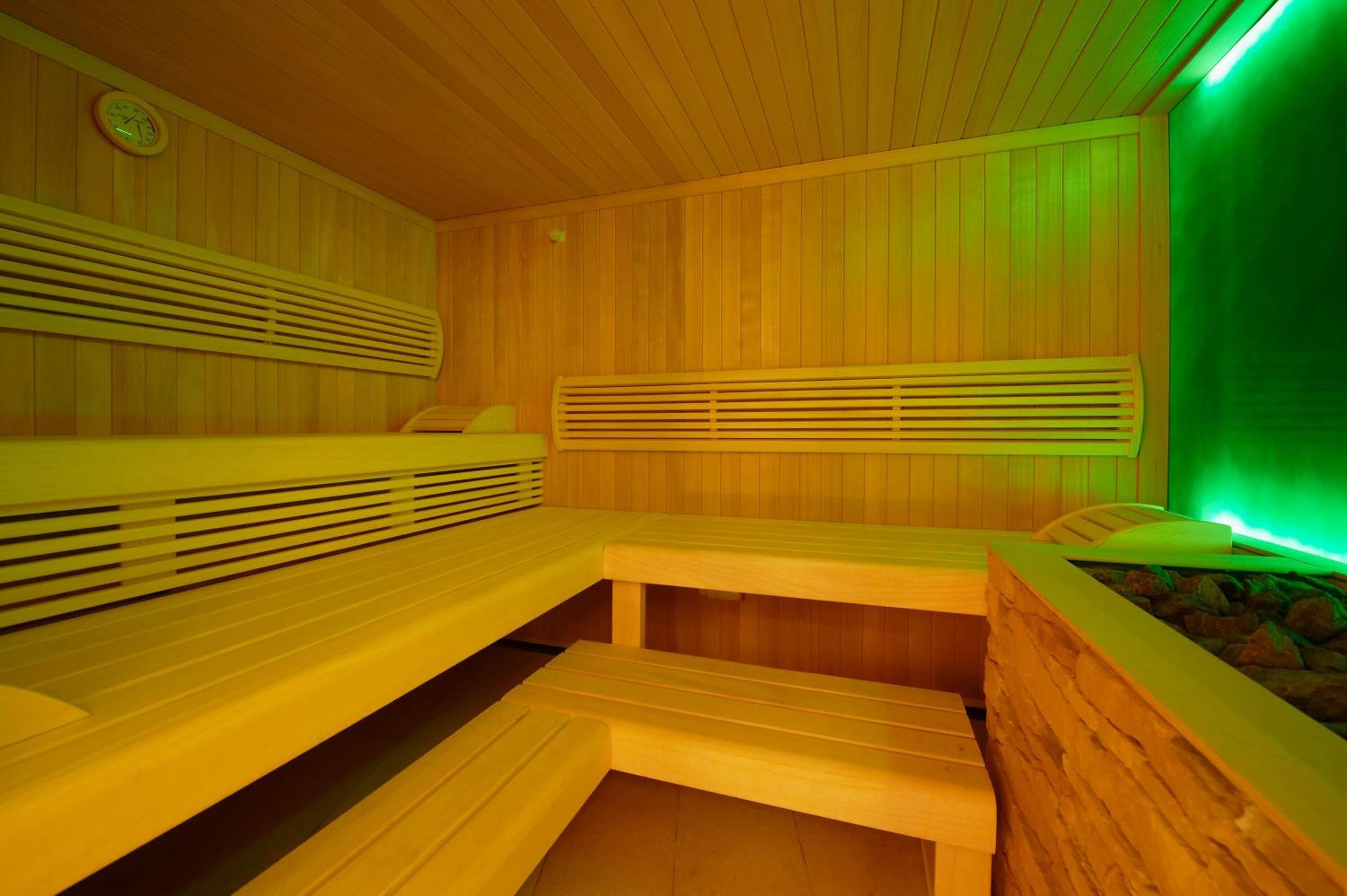 Un sauna avec des bancs en bois et un mur éclairé de lumière verte.