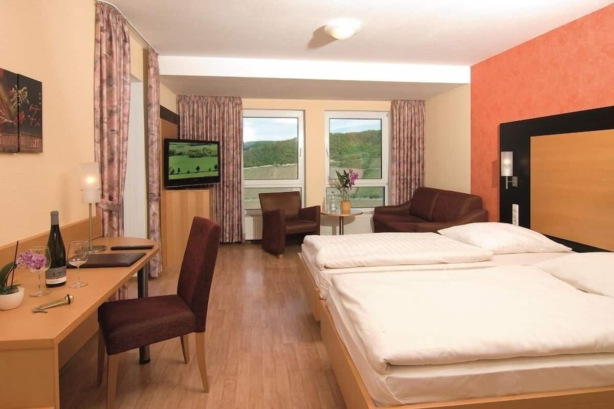 A hotel room with a bed, a desk with a chair, a television, and a window with a view of the countryside.