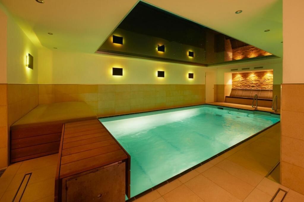 Ein moderner Innenpool mit einer Holzbank-Bereich, eingelassener Beleuchtung und einer Wand aus Stein.