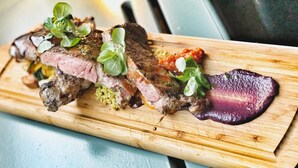 Une planche à découper en bois sur laquelle on voit de la viande tranchée, des légumes verts et une sauce violette.