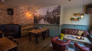 Un pub acogedor con paredes de ladrillo, un gran mural en blanco y negro, mobiliario de madera y una chimenea de ladrillo.