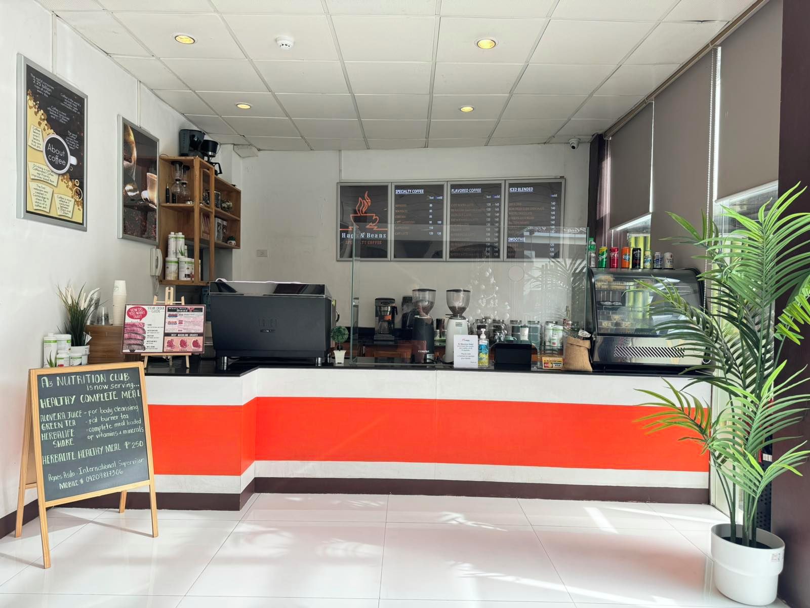 Interior de una cafetería con mostrador, máquinas de café y un panel de menú.
