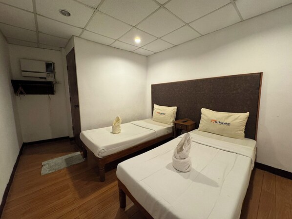 A hotel room with two beds, each with a pillow and a towel. There is a wooden floor, a ceiling light, and an air conditioning unit on the wall. - Sj Mansion Hotel (San Jose)