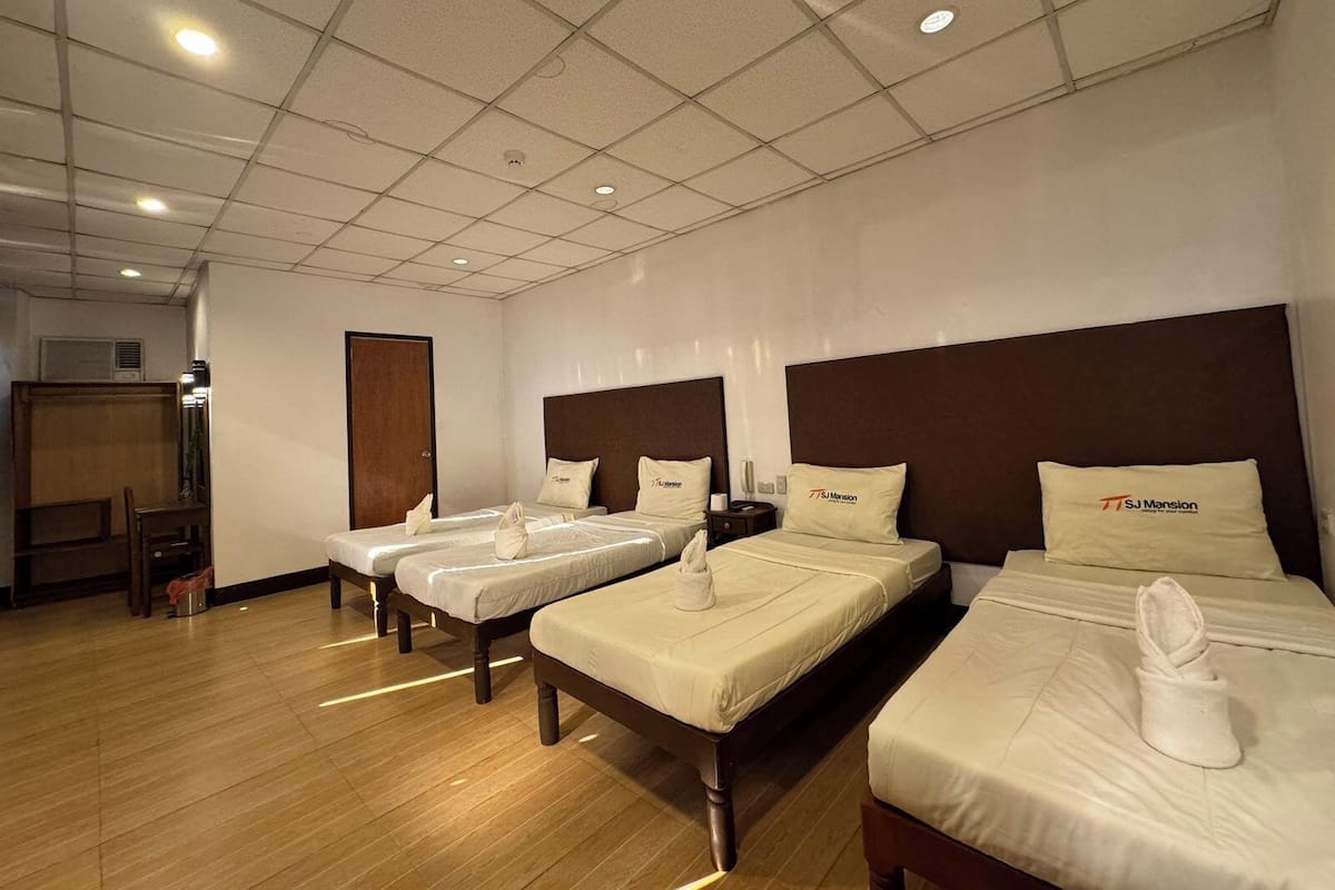 A hotel room with three beds, wooden headboards, and a tiled ceiling.