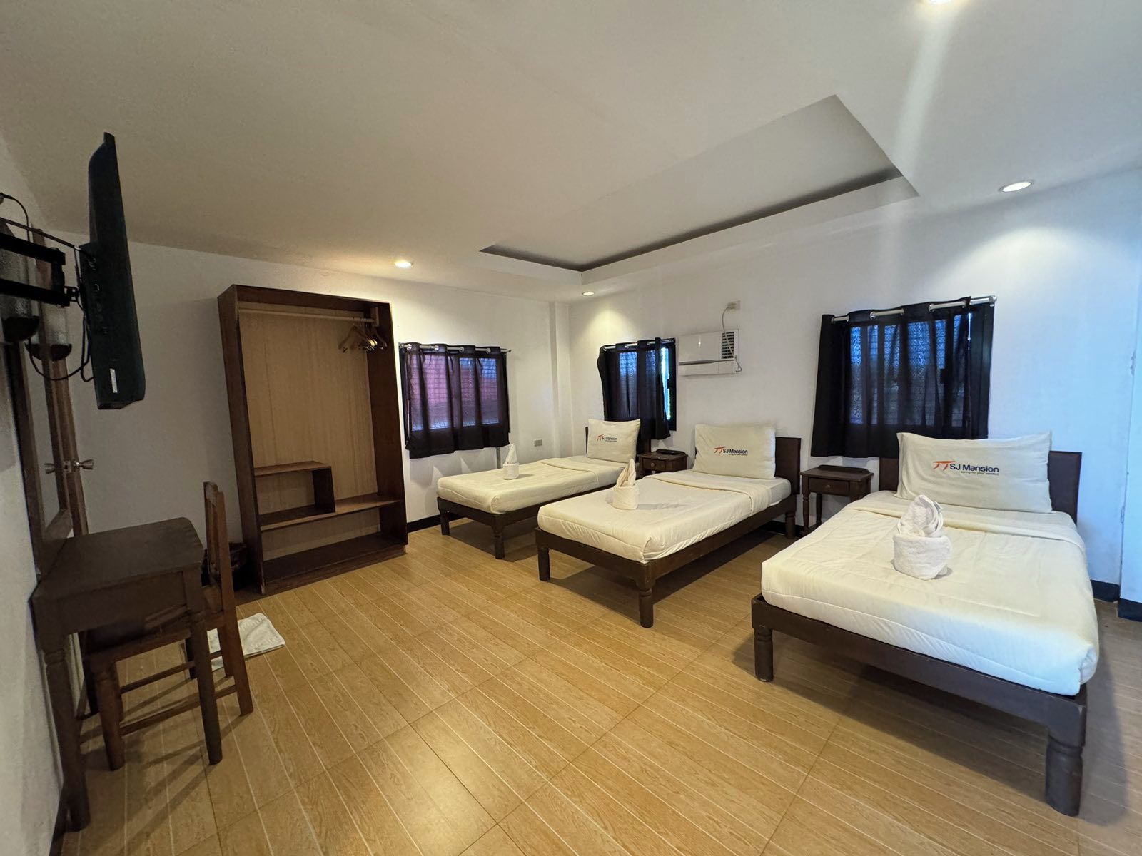 Habitación de hotel con dos camas individuales, un escritorio de madera, una silla, un televisor y un armario.
