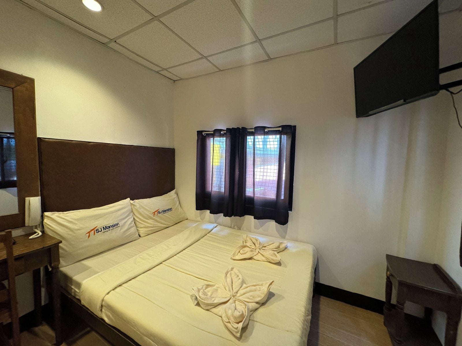 Une chambre d’hôtel avec un lit, une table de chevet, une télévision et une fenêtre avec des rideaux.