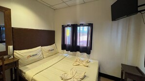 Ein Hotelzimmer mit einem Bett, einem Nachttisch, einem Fernseher und einem Fenster mit Vorhängen.