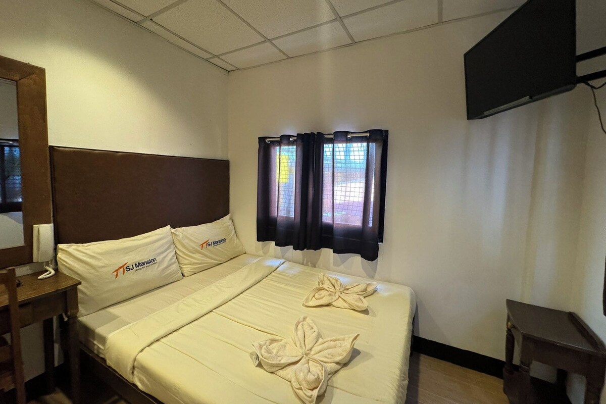 A hotel room with a bed, a nightstand, a TV, and a window with curtains.