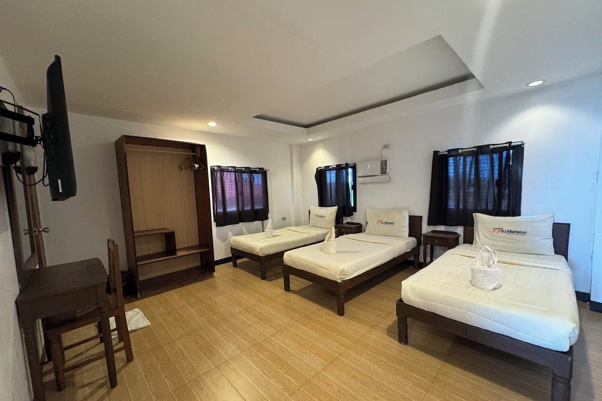 A hotel room with two single beds, a wooden desk, a chair, a TV, and a wardrobe.