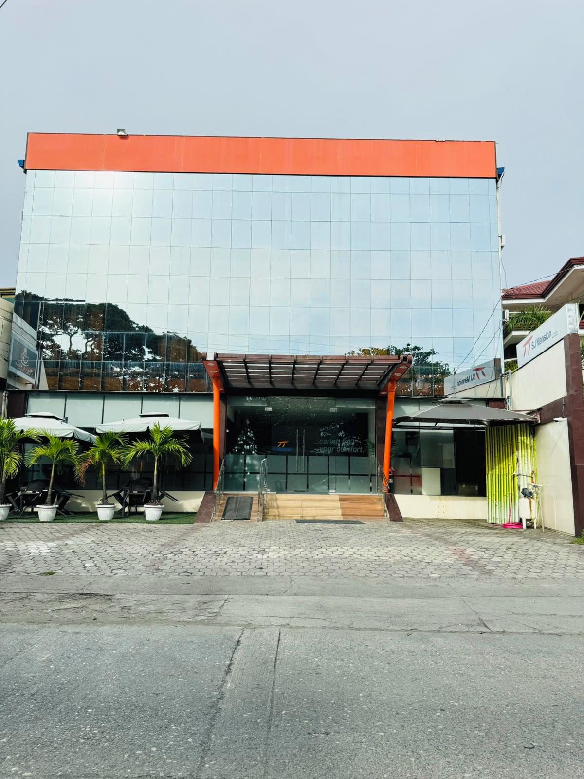 A modern building with a reflective glass facade, a red roof, and a covered entrance area with potted plants.