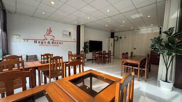 A spacious cafe interior with multiple wooden tables and chairs, a large plant, and a wall-mounted sign reading "Hugs & Beans Specialty Coffee".