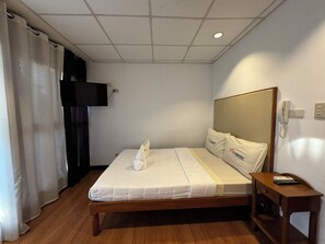 A hotel room with a wooden bed, white bedding, a bedside table with a phone, and a TV mounted on the wall.