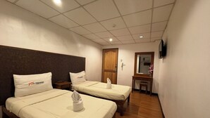 Ein Hotelzimmer mit zwei Betten, einem Holzkopfende, einem kleinen Schreibtisch, einem Spiegel und einem Fernseher an der Wand.
