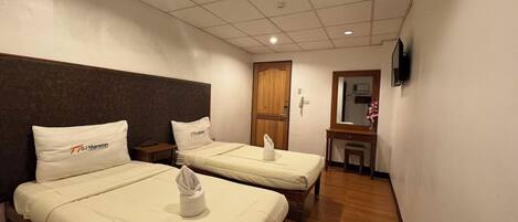 A hotel room with two beds, a wooden headboard, a small desk, a mirror, and a TV on the wall.