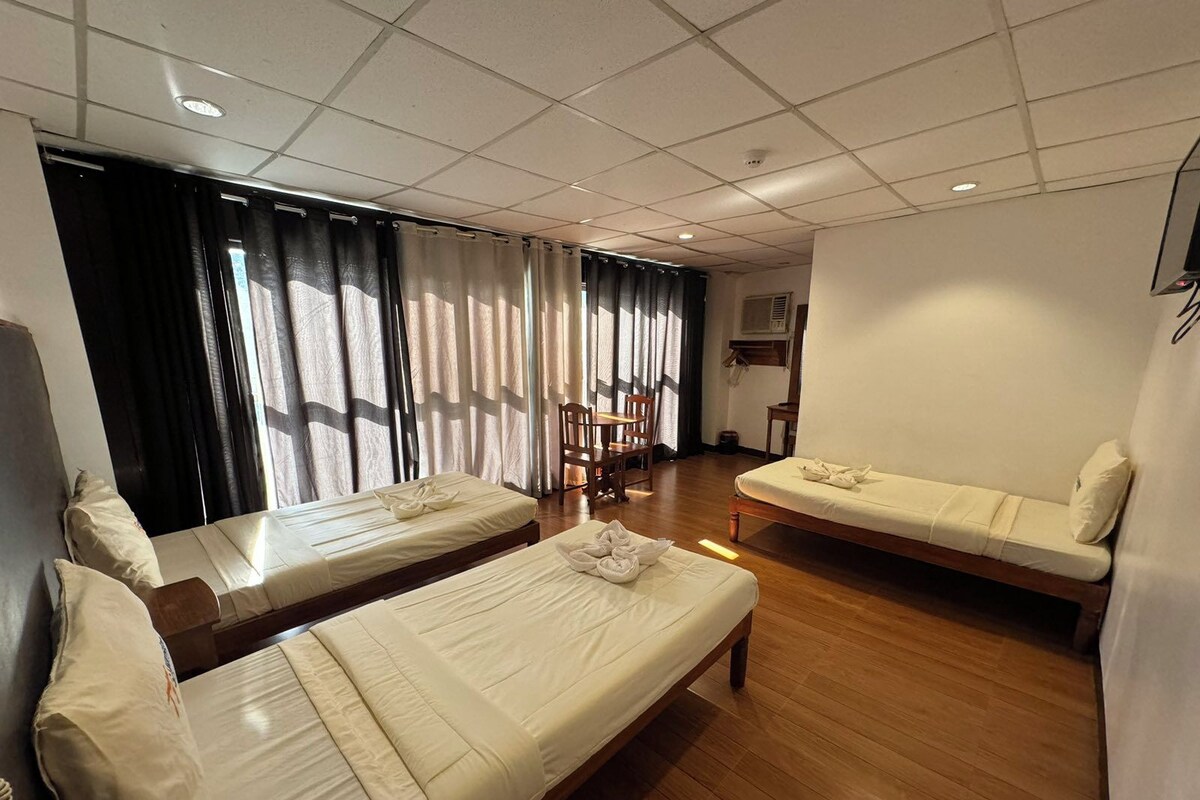 A hotel room with two single beds, a small table, and a chair.